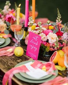 the table is set with pink and yellow flowers, plates, napkins, and candles