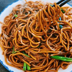 a plate full of noodles with chopsticks sticking out of the top, on a wooden table