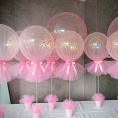 pink and white balloons are hanging from the ceiling above a table with cupcakes