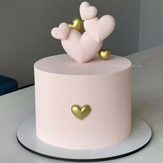 a pink cake with gold hearts on top and a white frosted cake stand next to it