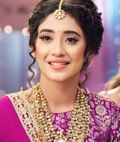 a woman in a purple outfit with gold jewelry on her neck and headpiece, smiling at the camera