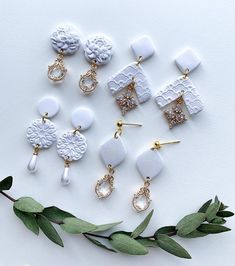 several white and gold earrings on top of a branch next to some green leafy branches