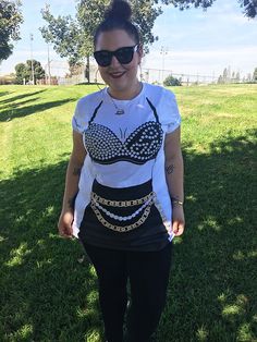 a woman standing in the grass wearing black and white clothing with chains around her waist