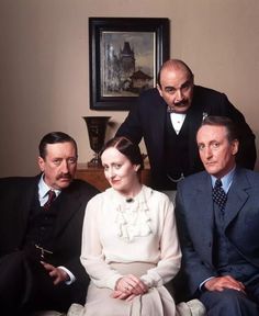 three men and a woman sitting on a couch in front of a man wearing a suit