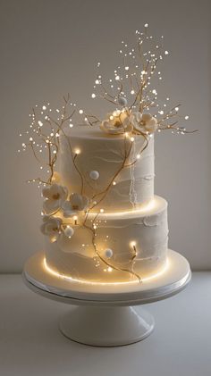 a three tiered cake with white frosting and flowers on top is lit up by fairy lights