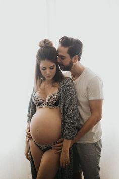 a man and woman standing next to each other in front of a window with their pregnant belly