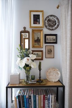 there is a shelf with books and pictures on the wall next to a vase filled with flowers