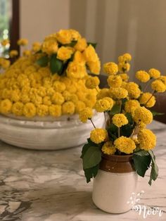 yellow flowers are sitting in small vases on a marble counter top, with green leaves