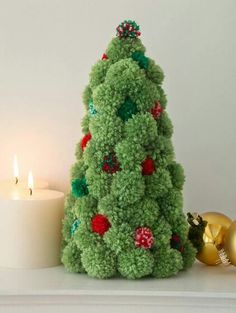 a green christmas tree sitting next to a lit candle on top of a white table