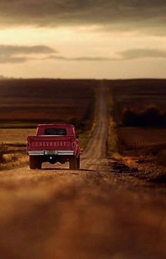 a red pick up truck driving down a dirt road in the middle of an open field