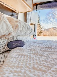 the mattress is in front of an open camper door with trees and snow on it