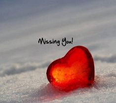 a red heart sitting in the snow with a message missing you on it's side