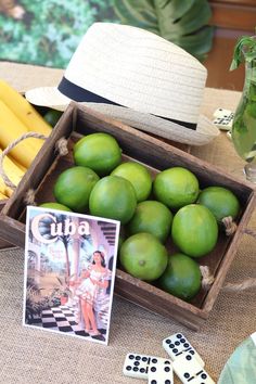 a wooden box filled with green fruit next to two dices and some banana's