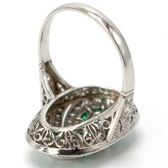 This jaw dropping ring, an Art Deco piece of art likely made in the 1920s, is made of platinum and features two central bezel set diamonds ensconced by an infinity-style figure eight channel of square cut emeralds. The rest of the ring's top contains multiple angular swirls of diamonds that are separated by pierced cut-outs, giving a palpable sense of motion to the piece. The shoulders are beautifully pierced and the undercarriage—or gallery—is ornately filigreed. Metal: Platinum Main Stones: 2 Platinum Oval Emerald Ring With 17 Jewels, Oval Platinum Emerald Ring With 17 Jewels, Platinum Emerald Ring In White Gold, Art Deco Emerald Ring In Platinum, Art Deco Platinum Emerald Ring, Oval Hallmarked Emerald Ring In Platinum, Hallmarked Oval Emerald Ring In Platinum, Art Deco Emerald Ring With 17 Jewels, Art Deco Emerald Ring With Platinum