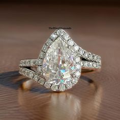 a pear shaped diamond ring on a wooden table with diamonds surrounding it and the band