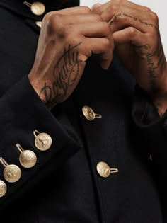 a man with tattoos on his arm and two gold studs in his lapel