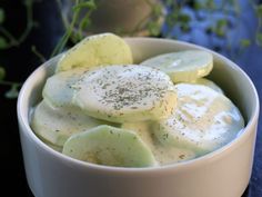 a white bowl filled with cucumber slices and cream cheese dressing on top of a blue table cloth