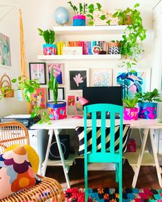 a room with plants and pictures on the wall, including a blue chair in front of a white desk