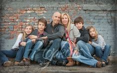 a family sitting on the ground in front of a brick wall with their arms around each other