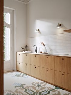 a kitchen with wooden cabinets and white tile on the floor, along with an area rug