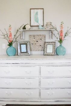 a white dresser topped with pictures and vases filled with flowers on top of it