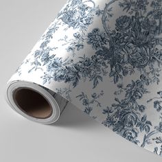 a blue and white floral wallpaper with leaves on it's side, next to a roll of paper