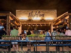 people sitting at tables in front of a restaurant with lights on the roof and windows