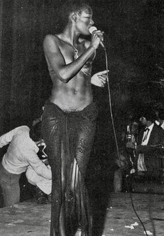 a man with no shirt on standing in front of a microphone and singing into a mic