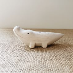 a small white ceramic animal sitting on top of a brown cloth covered floor next to a wall