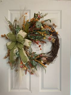 a wreath is hanging on the front door with flowers and leaves around it, as well as a bow