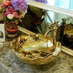 a gold sink sitting on top of a marble counter next to a vase filled with flowers