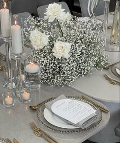 the table is set with silverware and white flowers in vases, candles, and menu cards