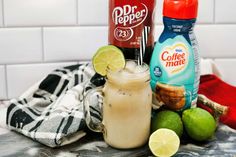 two bottles of iced coffee and limes on a counter with a plaid towel next to them