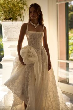 a woman in a white dress standing next to a window