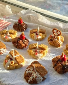 many cookies and pastries are arranged on a white tablecloth, with pretzels sticking out of them