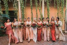 a group of women standing next to each other in dresses and holding bouquets with greenery on the wall behind them