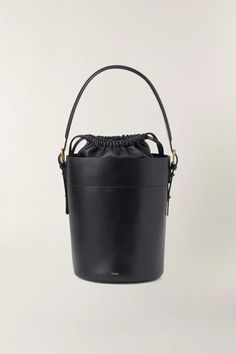 Black leather bucket bag- Hand, shoulder, or cross-body bag- Golden metallics- Fastens with an inner leather drawstring pouch- Height 26 cm, depth 18 cm- One removable leather handle - length 77 cm - One removable cotton handle - length 106 cm Luxury Modern Pouch Bucket Bag, Luxury Modern Bucket Bag With Removable Pouch, Luxury Black Bucket Bag With Leather Lining, Black Bag Bucket, Luxury Handmade Black Bucket Bag, Black Leather Bucket Bags, Luxury Black Bucket Bag With Multiple Compartments, Black Bucket Handbag, Luxury Modern Black Bucket Bag