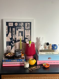 a table topped with books and toys next to a painting on the wall behind it