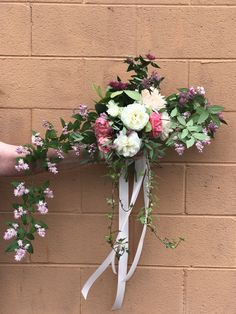 a bridal bouquet with pink and white flowers hanging from a ribbon on a brick wall