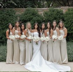 a group of women standing next to each other in front of trees and bushes holding bouquets