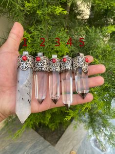 a person is holding five different types of pendants in their hand with red stones on them