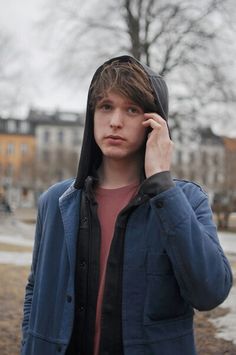 a young man wearing a hoodie talking on a cell phone while standing in a park