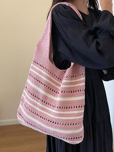 a woman holding a pink crocheted bag in her right hand while standing next to a wall