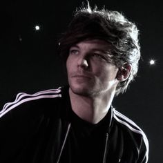 a man with long hair wearing a black jacket and earphones in front of a dark background