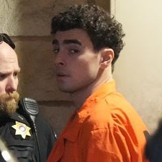 two men standing next to each other in an orange prison uniform and one man with a beard