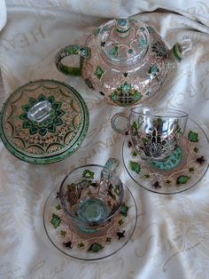 four pieces of glass sitting on top of a white cloth covered tablecloth with green and gold designs