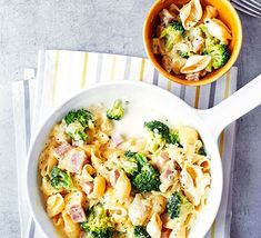 a bowl of pasta with ham and broccoli next to a fork on a napkin