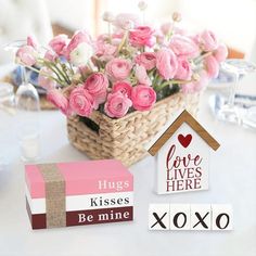 pink roses are in a basket next to some books and a house shaped sign that says hugs, kisses, be mine