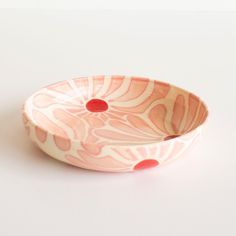 a pink and white bowl sitting on top of a white table next to a red dot