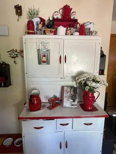 an old fashioned kitchen with red accents and white cupboards on the top, is shown